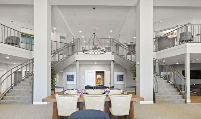 high ceiling lounge room with wooden accents, ample seating, a TV and community table among other social areas